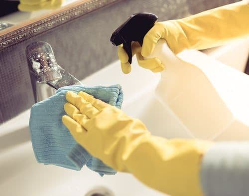 Gloved hands wiping down a bathroom sink and faucet during a deep cleaning