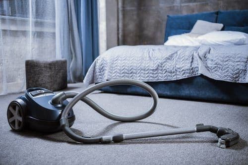 Vacuum cleaner on soft grey bedroom carpet before a professional carpet cleaning