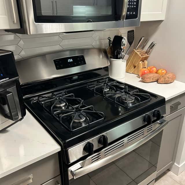 Gas range and stainless microwave wiped down, with a knife block and fruit bowl on the white counter — Ferrer Cleaning, Chicago, IL